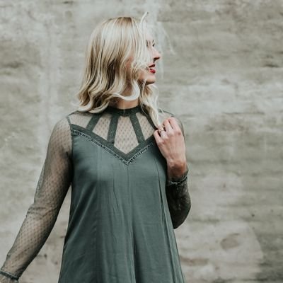 Blonde woman in green top touching hair and gazing to the right.