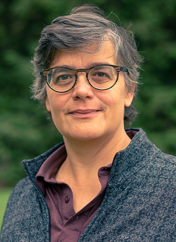 Photo of Ellen McCallum. Middle aged woman with glasses, short heathered black and grey hair, wearing a grey quarter zip.