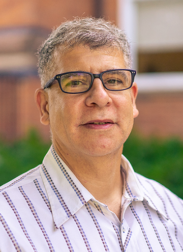Photo of Salah Hassan. Portrait of older middle aged man with glasses, short grey hair, and wearing striped white button up.