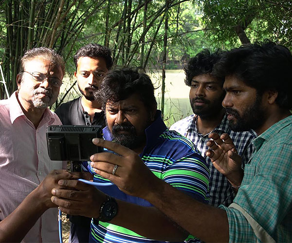 Five men gather around a camera to look at what its displaying. They all have black hair.