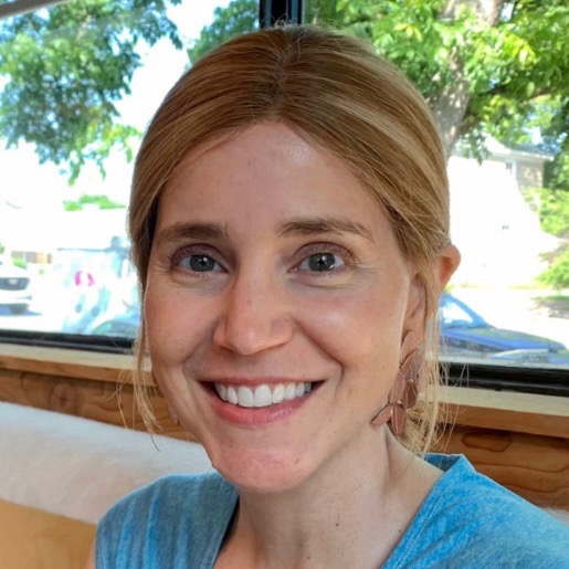 A outdoor portrait of a smiling woman with blonde hair wearing a blue top.