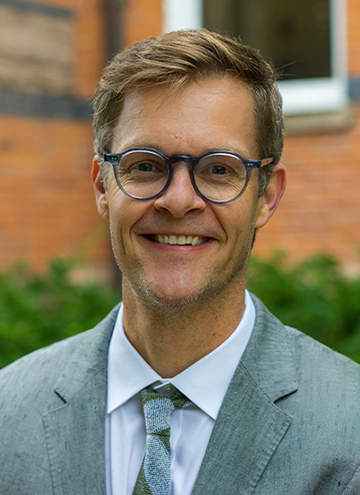 Photo of Justus Nieland. Young middle aged man with light brown hair and glasses, wearing a grey suit coat.
