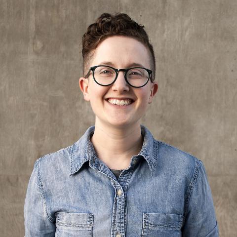 Woman with short hair and black glasses in denim shirt smiling at camera.