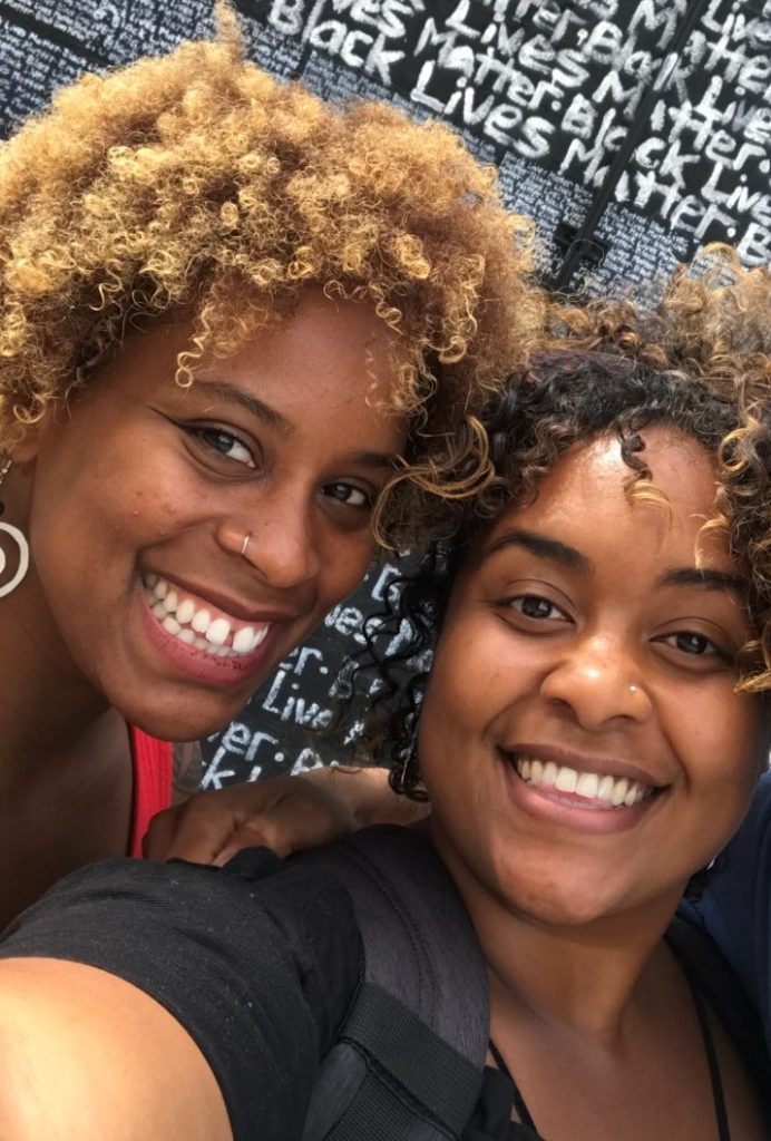 image of two woman smiling at the camera with 'Black Lives Matter' written in white lettering all over the background