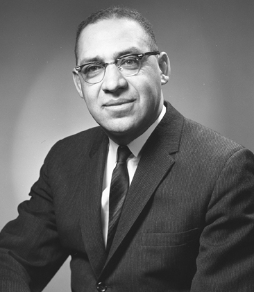 a black and white image of a man wearing glasses in a suit