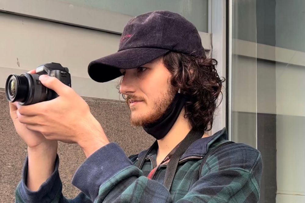 Young man in hat holds camera.