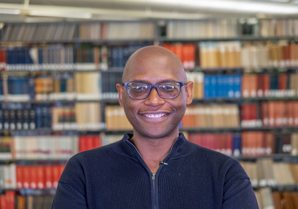 MSU Professor of English Julian Chambliss smiles in a portrait with books on bookshelves in the background.
