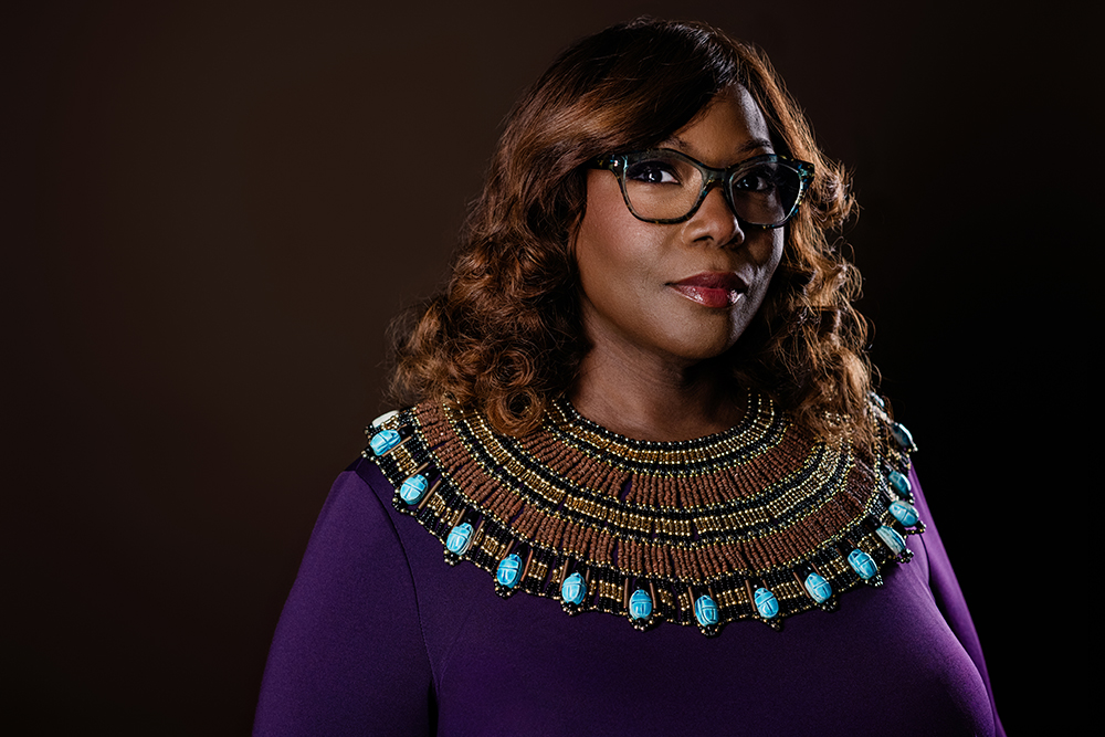 Portrait of a woman wearing glasses, a purple dress, and a colorful beaded collar necklace.