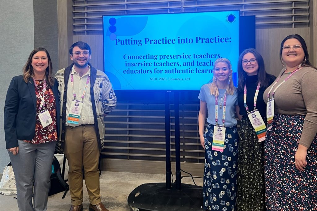 Five people standing next to a TV monitor that says: “Putting Practice into Practice: Connecting Preservice Teachers, Inservice Teachers, and Teacher Educators for Authentic Learning."
