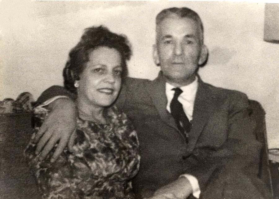 A black and white photo of a man and a woman who are sitting and the man has his arm around the woman. 