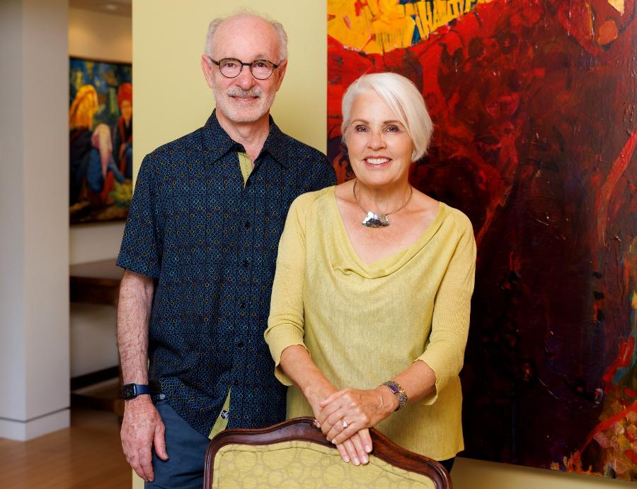 A man and a woman standing with a brightly colored painting in the background. 