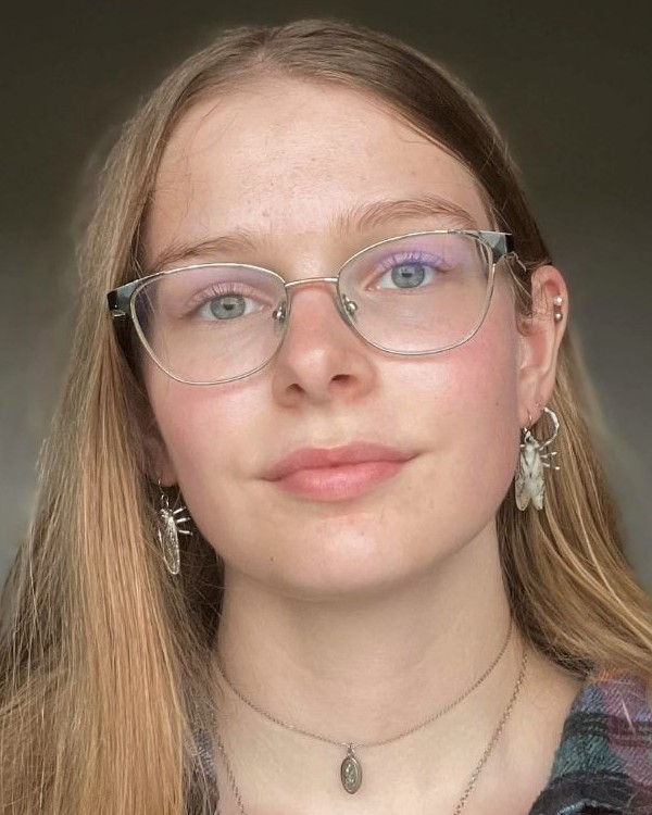 A picture of a person with blond hair, silver earrings, and glasses smiling