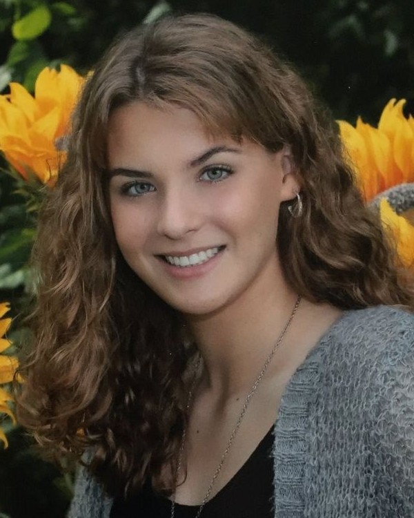 A picture of a person with long brown hair and a grey sweater, in front of a background of flowers